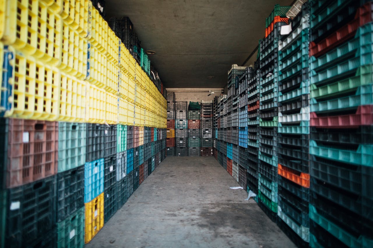 Empty passage with cement floor between heaps of colorful plastic boxes and pallets in rows in warehouse